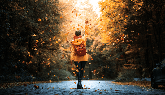 top fall 2024 destinations woman standing in middle of road as leaves fall around her looks like autumn